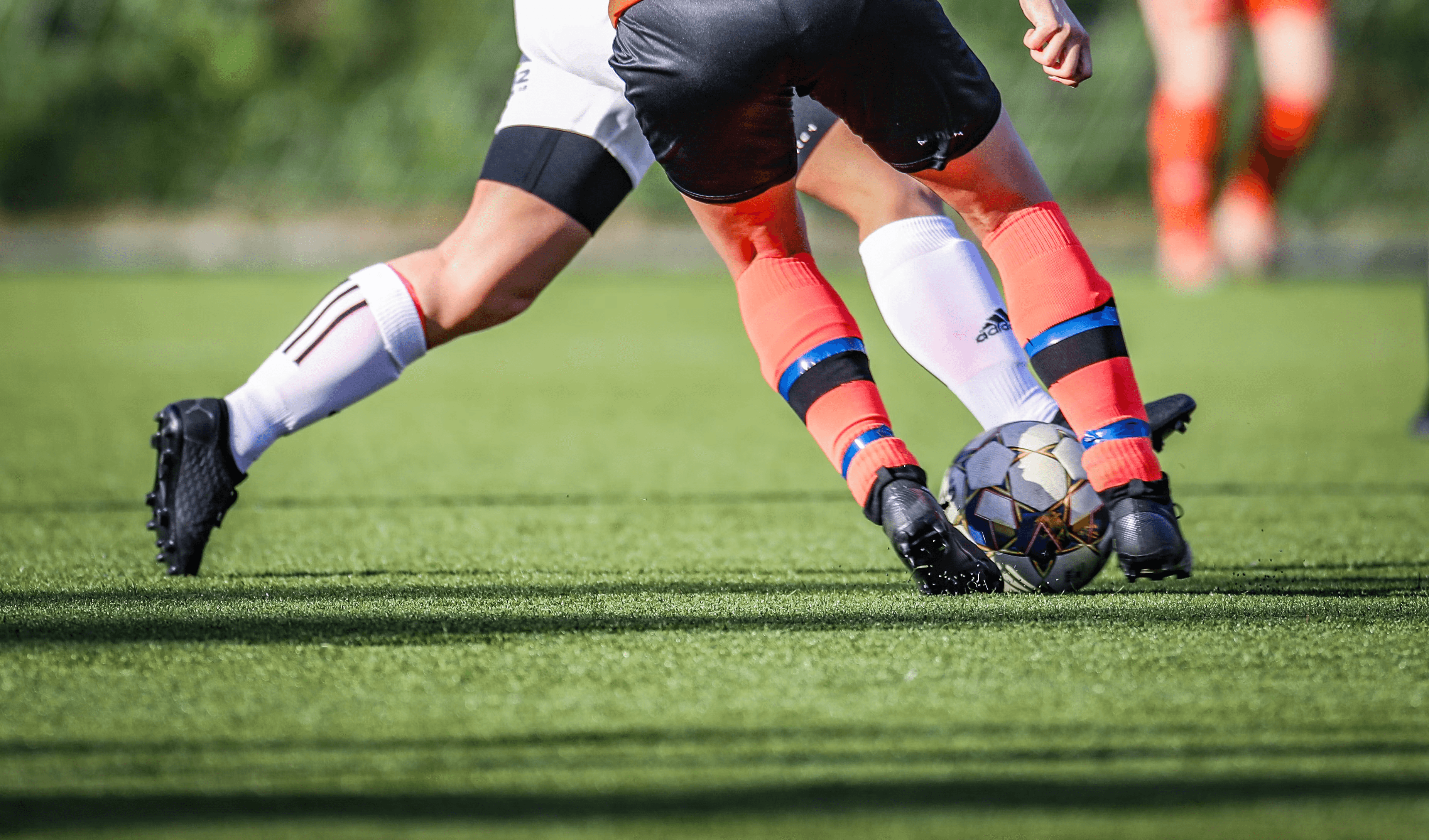 Close-up of a soccer cleat resting on a football on a grass pitch